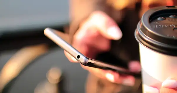 Mains tenant un smartphone Android à côté d’une tasse de café